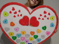 Drugie zdjęcie przedstawia Zuzannę Termolik dziewczynkę w okularach trzymającą duże kartonowe serce na tle którego znajdują się mniejsze serduszka wypełnione różnokolorowymi guzikami